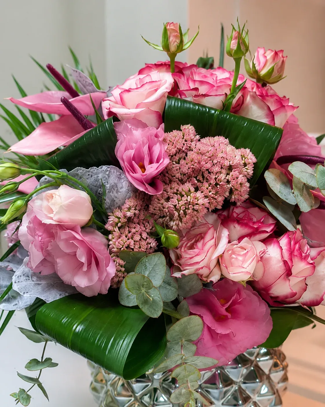 Pembe güller, pembe anthurium formunda çiçekler, okaliptüs ve parlak yeşil yapraklarla cam vazoda hazırlanmış zarif çiçek aranjmanı
