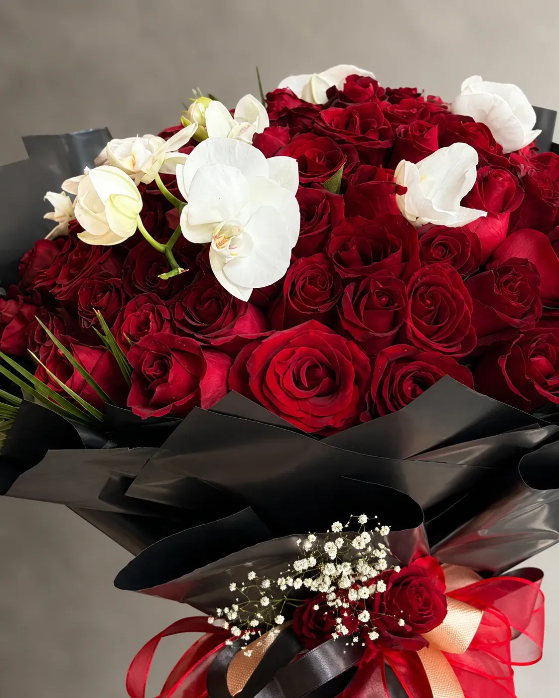 Siyah ambalaj içinde kırmızı güller ve beyaz orkide çiçekleriyle hazırlanmış premium romantik buket