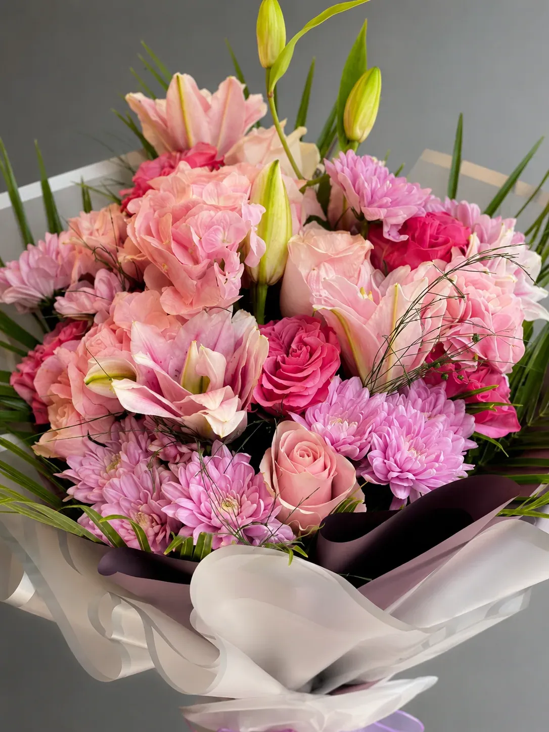 Pembe lilyum, pembe ve fuşya güller ile yeşil yapraklardan oluşan şık ambalajlı buket çiçek